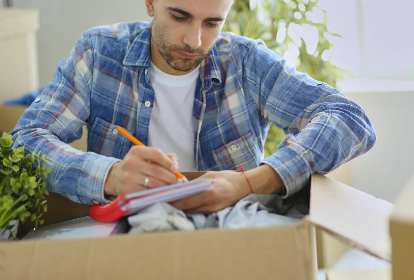Mover seated among packed boxes checking a furniture inventory list