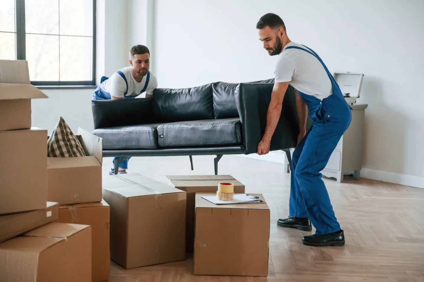 Two Stanford Van Lines movers lifting a sofa together in a living room