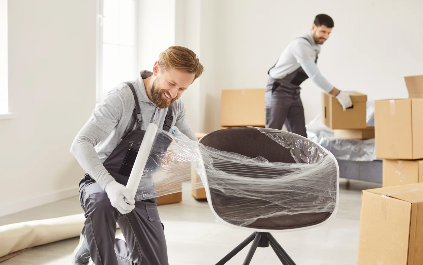Movers wrapping furniture in protective plastic beside stacked boxes